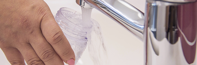 Lähikuvassa lasia pitelevä käsi laskemassa vettä hanasta.
