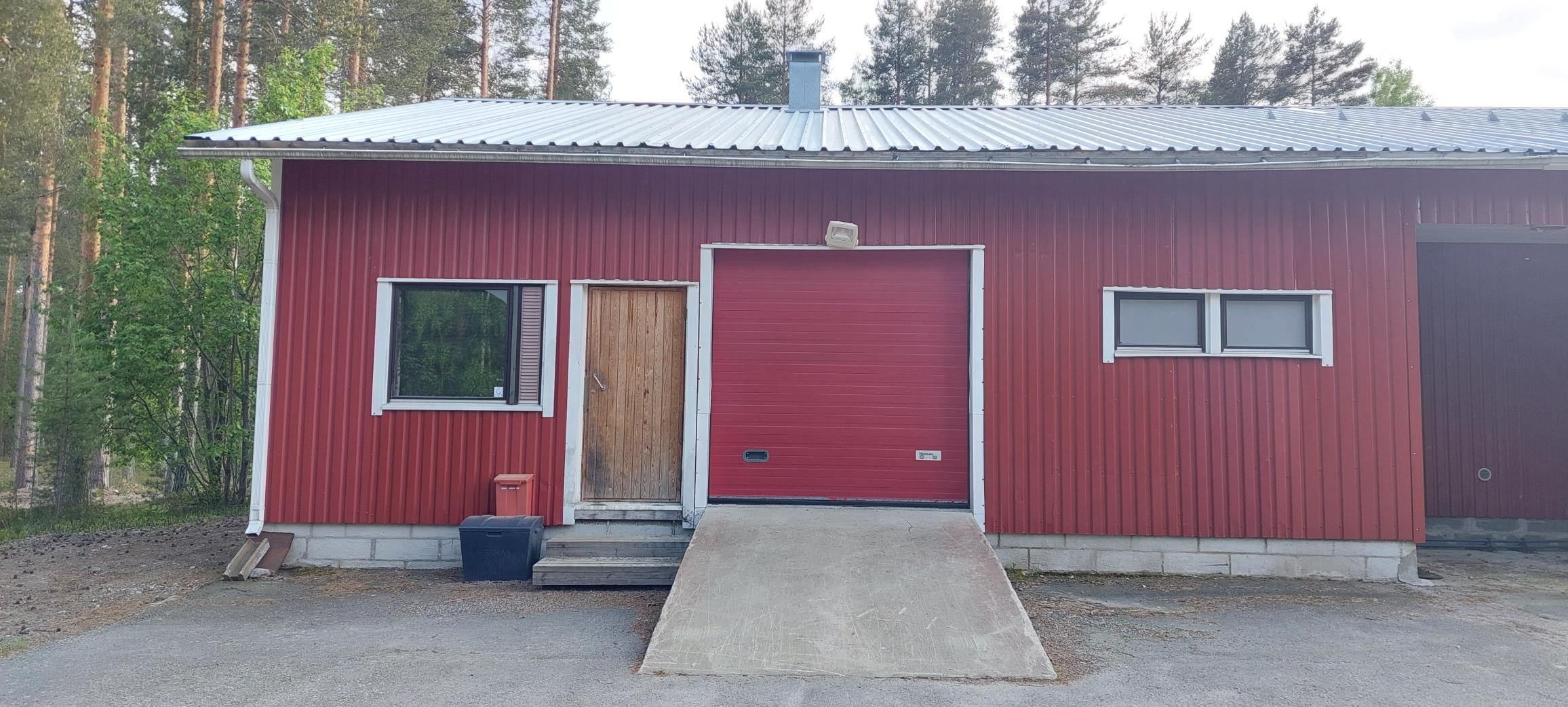 Punaisen rakennuksen julkisivu, jossa tavallinen käyntiovi sekä nosto-ovi ajoneuvoille