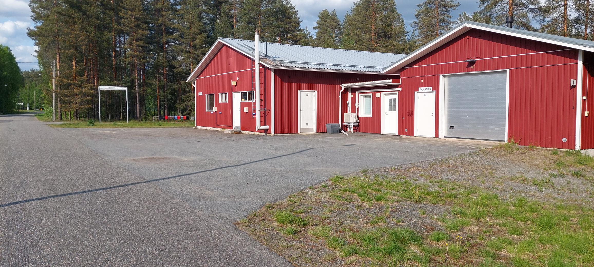 Punaisen rakennuksen julkisivu, jossa oikeassa reunassa korkea, metallinvärinen nosto-ovi, keskellä ikkuna ja kaksi valkoista käyntiovea ja vasemmassa päädyssä jälleen korkeampi halliosa.